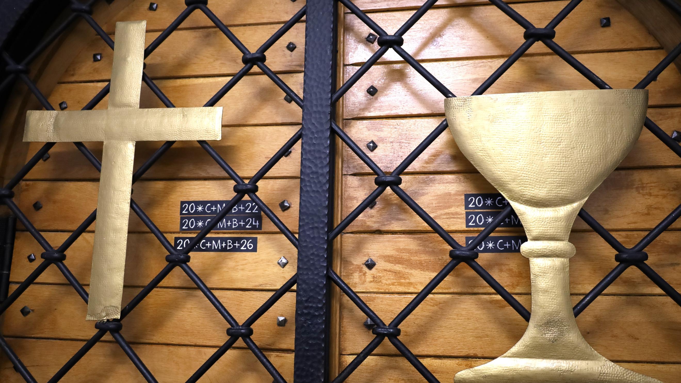Tür zur Kapelle der JVA Saarbrücken mit goldenem Kreuz und Kelch vor schwarzem Gitter