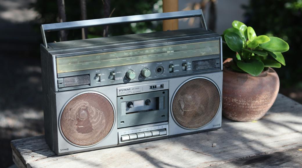 Neben einem alten Radio aus geschätzt den Achtzigern steht eine kleine grüne Pflanze in einem Tontopf