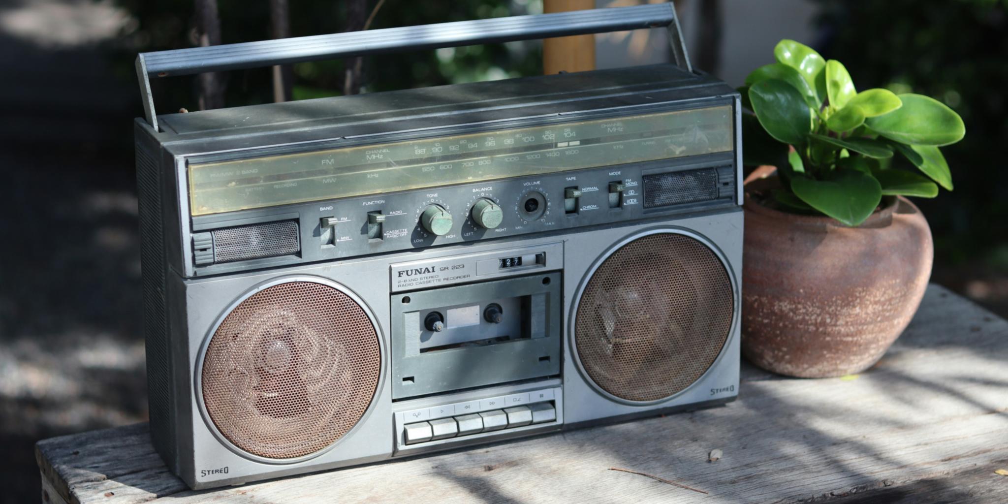 Neben einem alten Radio aus geschätzt den Achtzigern steht eine kleine grüne Pflanze in einem Tontopf