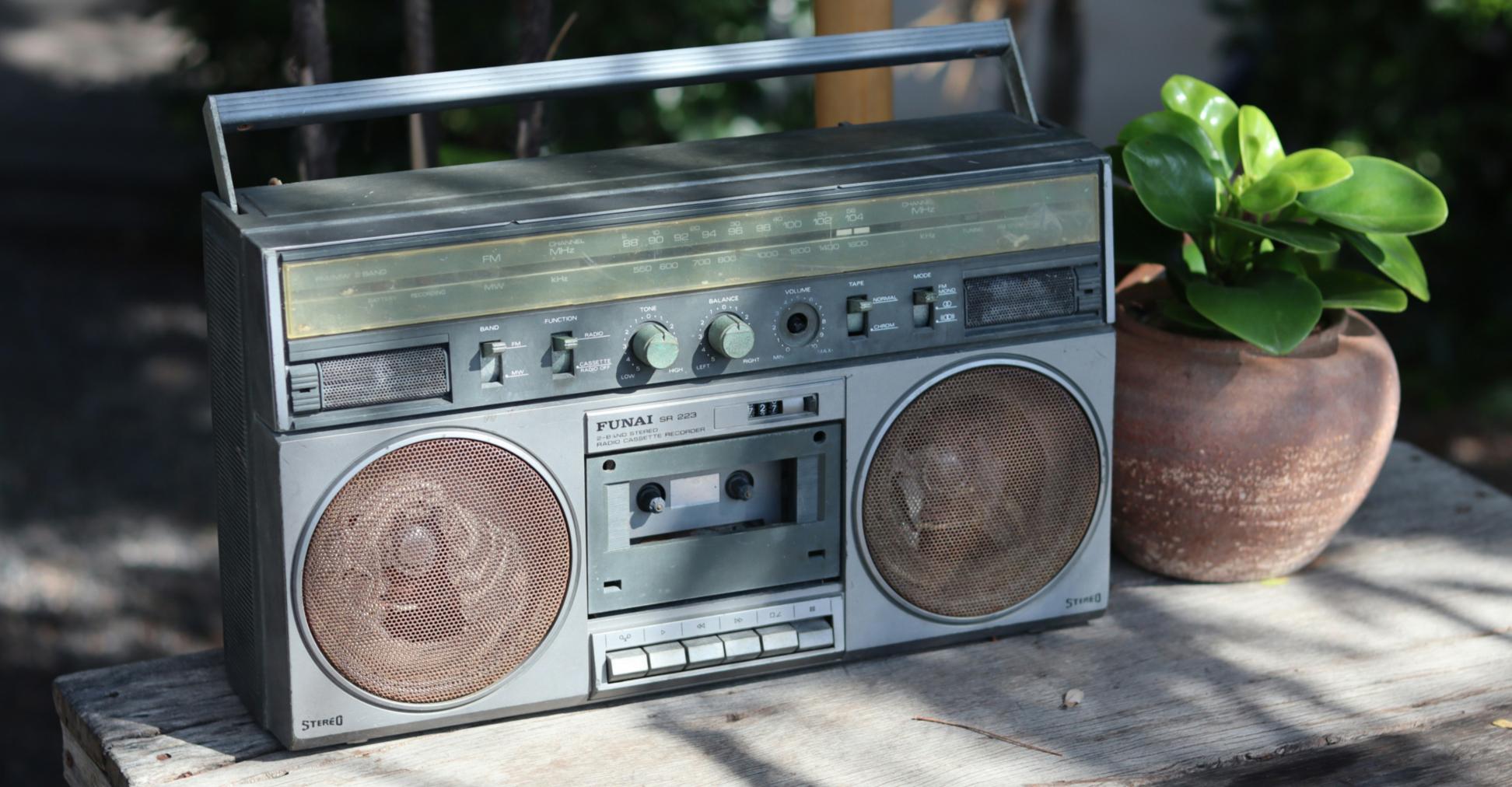Neben einem alten Radio aus geschätzt den Achtzigern steht eine kleine grüne Pflanze in einem Tontopf