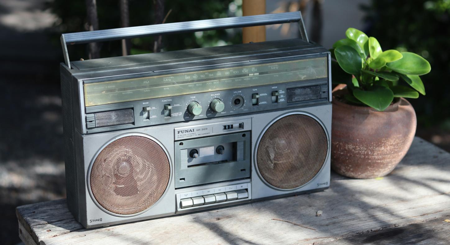 Neben einem alten Radio aus geschätzt den Achtzigern steht eine kleine grüne Pflanze in einem Tontopf